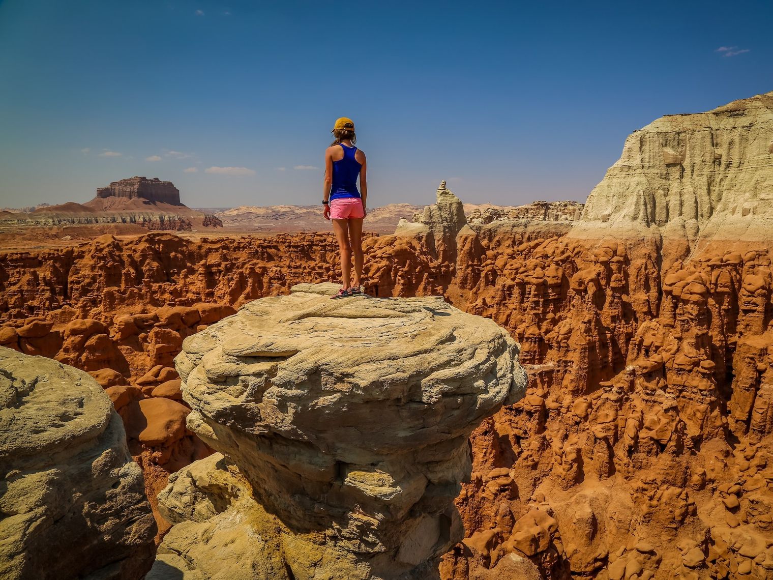 Ein Wanderer steht auf einem Felsvorsprung und überblickt die geformten roten Felsformationen und die Wüstenlandschaft des amerikanischen Südwestens.