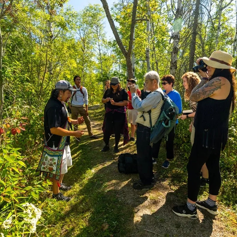 Groep reizigers aandachtig luisterend naar en verhaal van een First Nations gids, midden in de natuur van Wiikwemkoong.