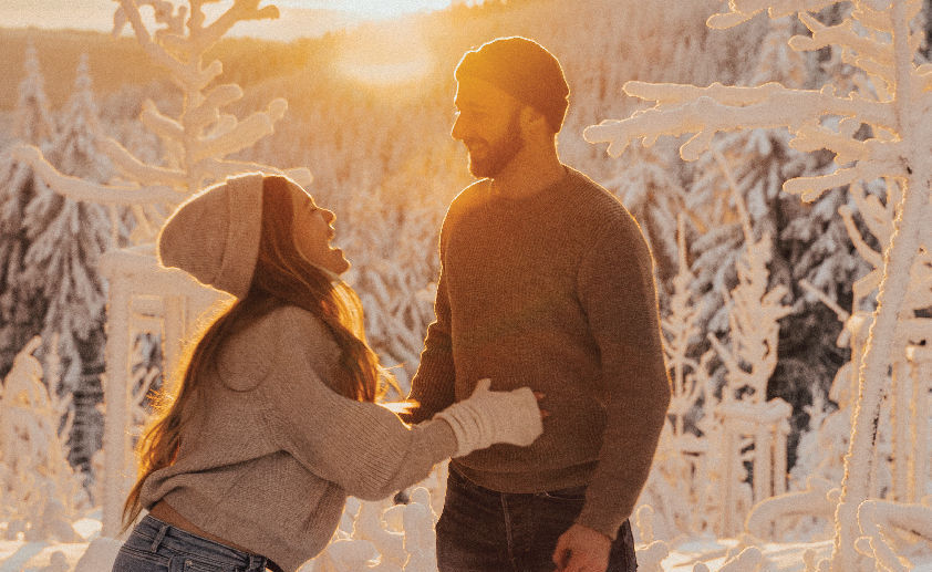 A man and woman are standing in a snowy forest.