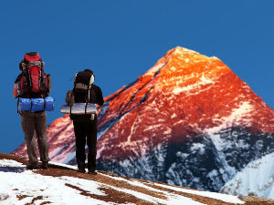 Two people with backpacks standing on top of a snowy mountain.