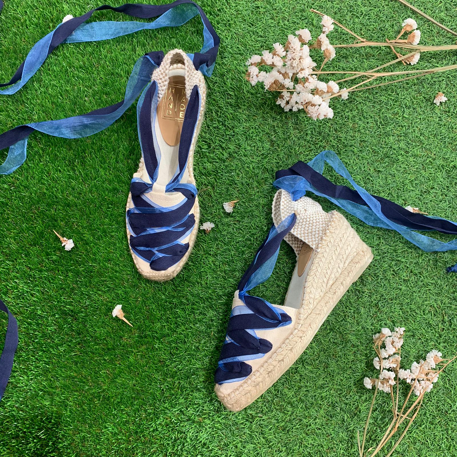 A pair of blue espadrilles on grass with ribbons.