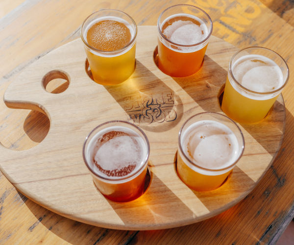 Five glasses of beer on a wooden tray.