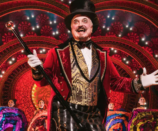 A man in a top hat is holding a baton in front of a stage.