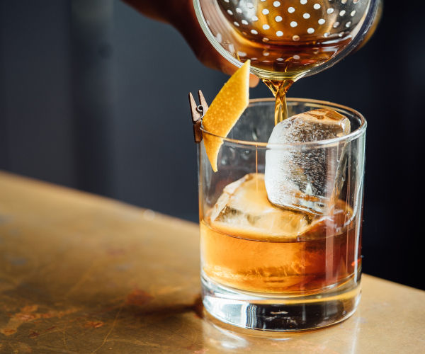 A person pouring an old fashioned into a glass.