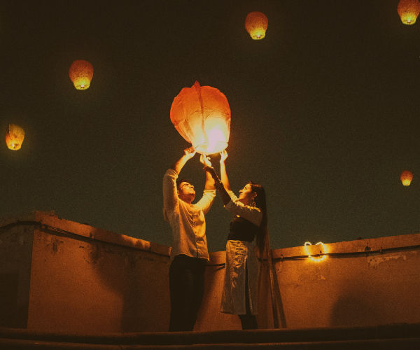 Couple holding lanterns in the sky at night.