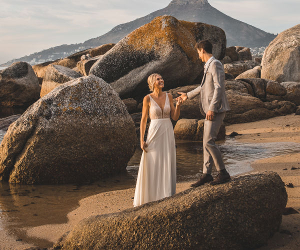 Bride and groom standing on rocks in front of table mountain.