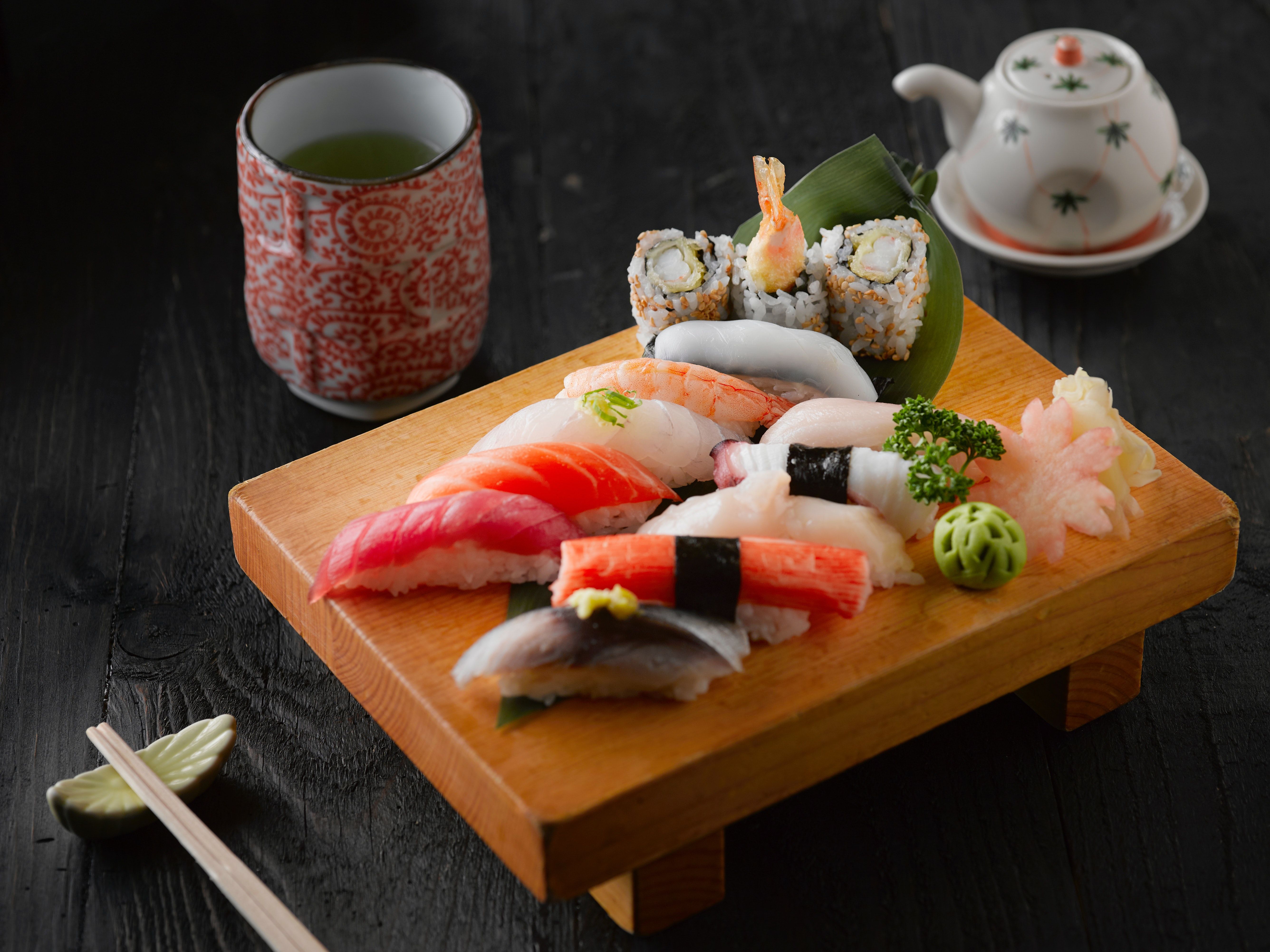 A wooden cutting board with sushi and a cup of tea.