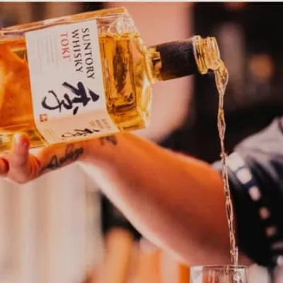 A bottle of Suntory Whisky Toki is being poured into a glass, showcasing its golden hue.