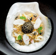 A dish with caviar and black olives on a black plate.