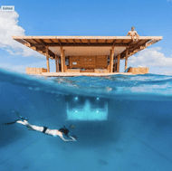 A person snorkling under the water in front of a house.