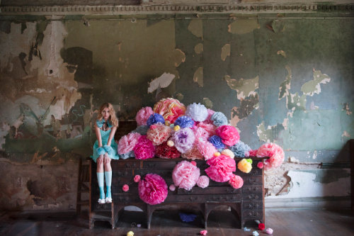 A girl sits in front of a pile of colorful paper pom poms.