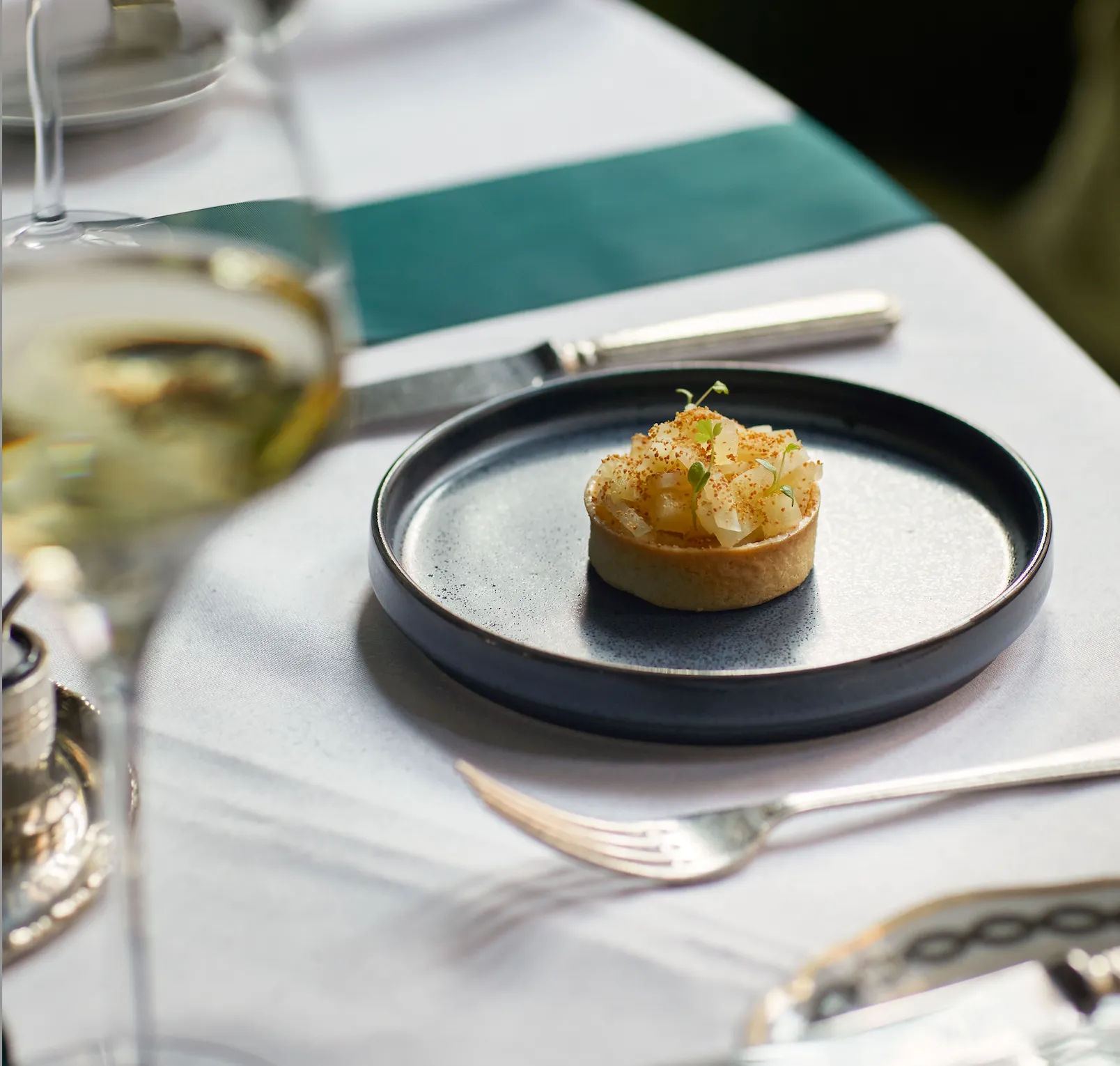 A small tart on a plate next to a glass of wine.