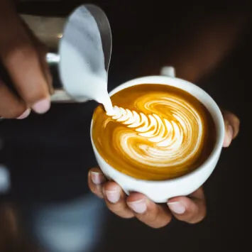 A person pouring latte into a cup of coffee.