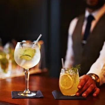A bartender holding two glasses of gin and tonic