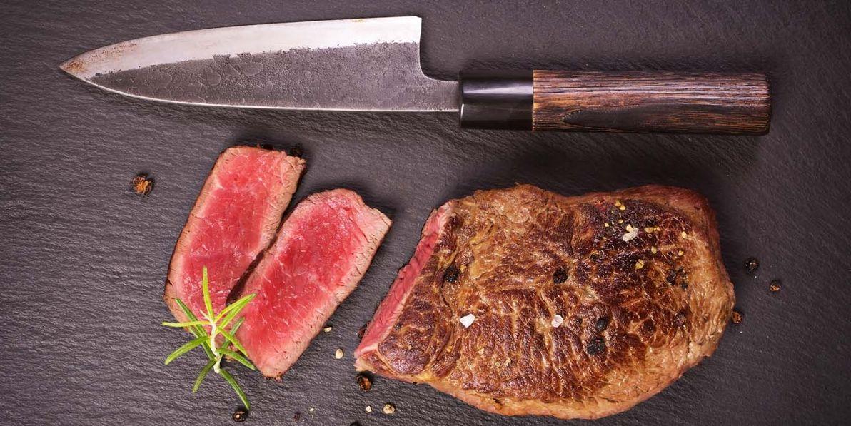 A piece of steak and a knife on a black surface.