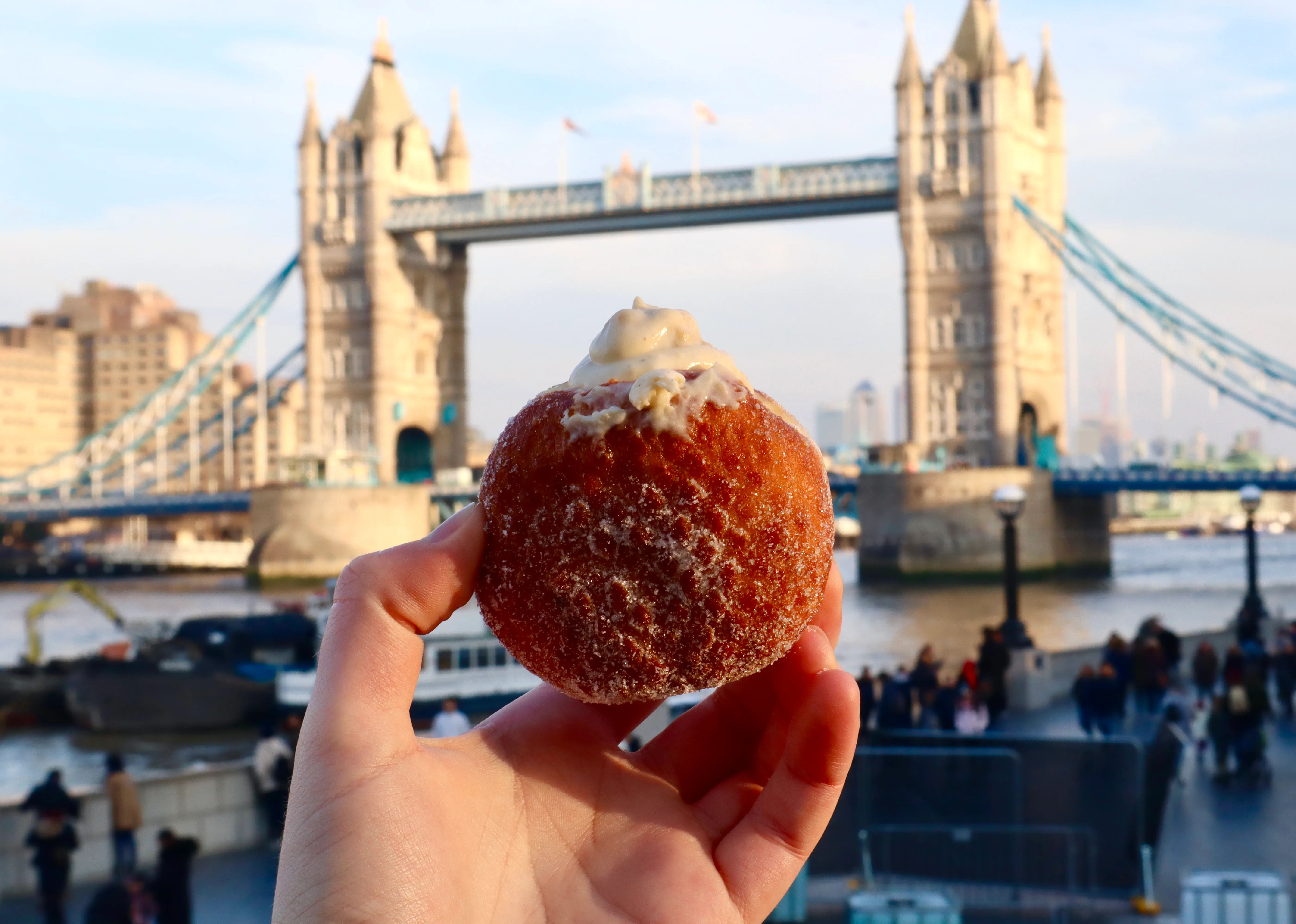 A person holding a donut in front of tower bridge.