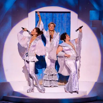 Three women in silver costumes standing on stage.