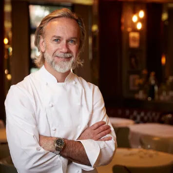 A chef standing in a restaurant with his arms crossed.