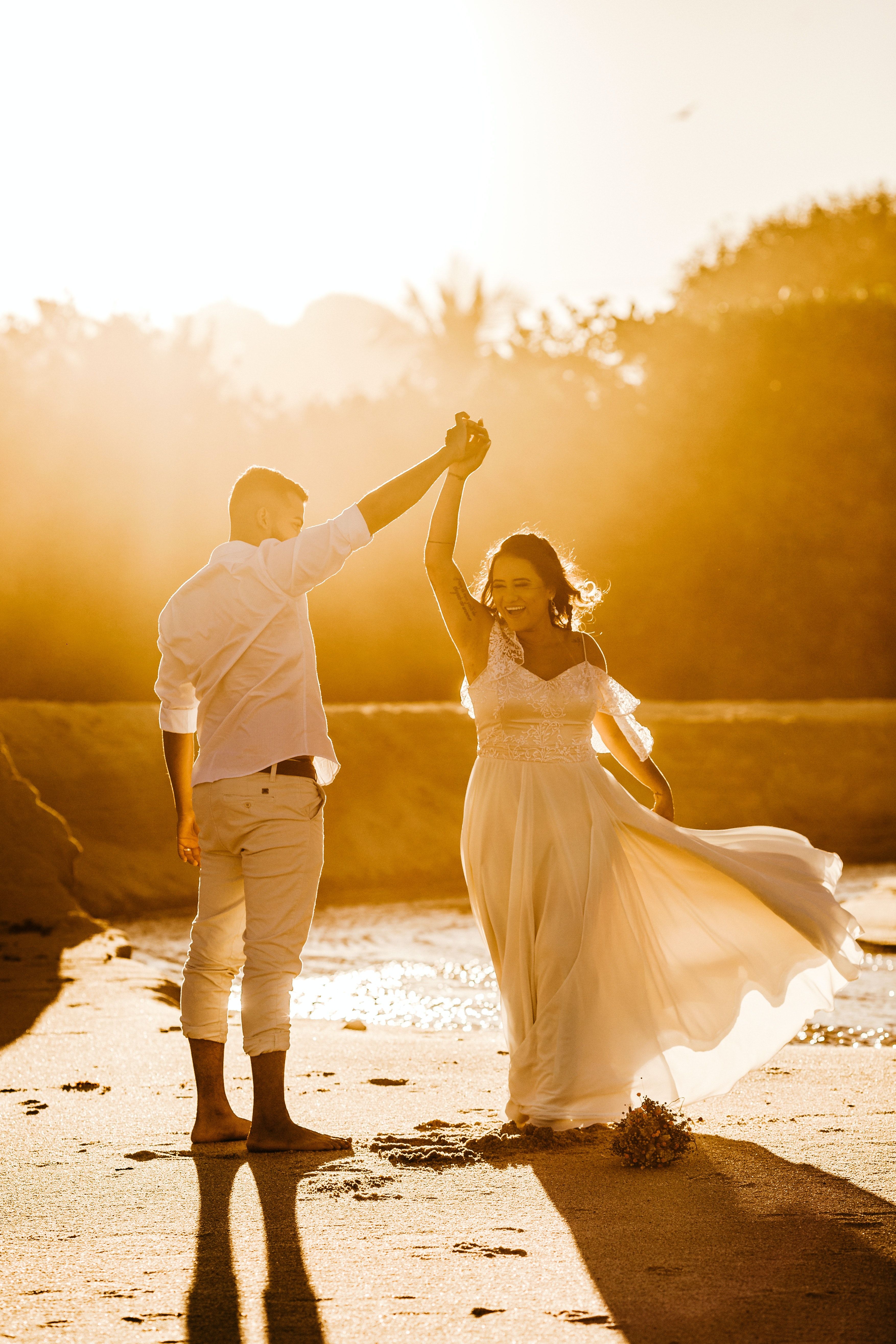 A bride and groom dancing on the beach at sunset.