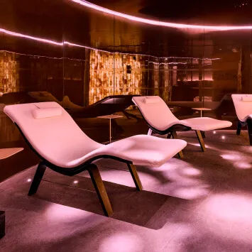 Four lounge chairs in a room with pink lighting