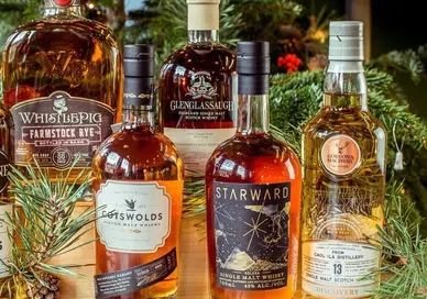 A collection of whisky bottles in front of a Christmas tree.