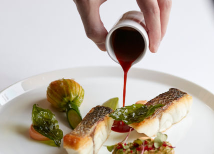 An image of a person pouring sauce on a plate, 7-Course Tasting Menu. Marcus