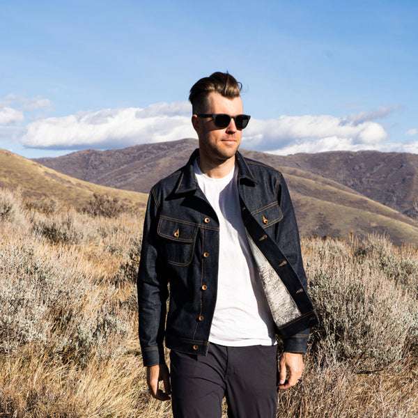 A man standing in a field wearing a denim jacket