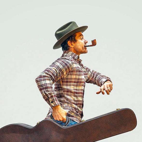 A man walking with a guitar while smoking a pipe