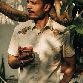 fit model wearing The Embroidered Short Sleeve Western in Natural, holding mug, cropped shot 