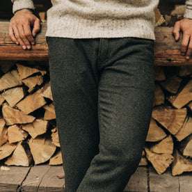 fit model wearing The Camp Pant in Dark Moss Wool, sitting against wood 