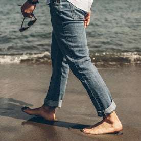 Our fit model walking along the sea shore in twenty-four wash slim cut denim jeans
