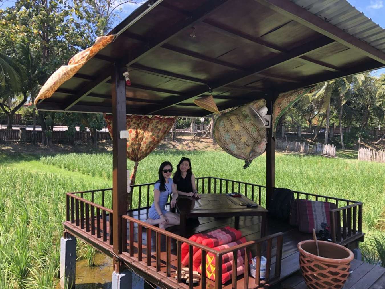 two women sitting in a hut at the middle of a paddy field