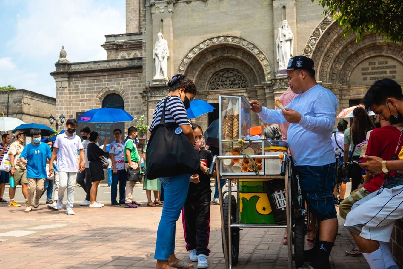 Tourists buy ice cream from vendors in front of Manila Cathedral using language Ilocano 