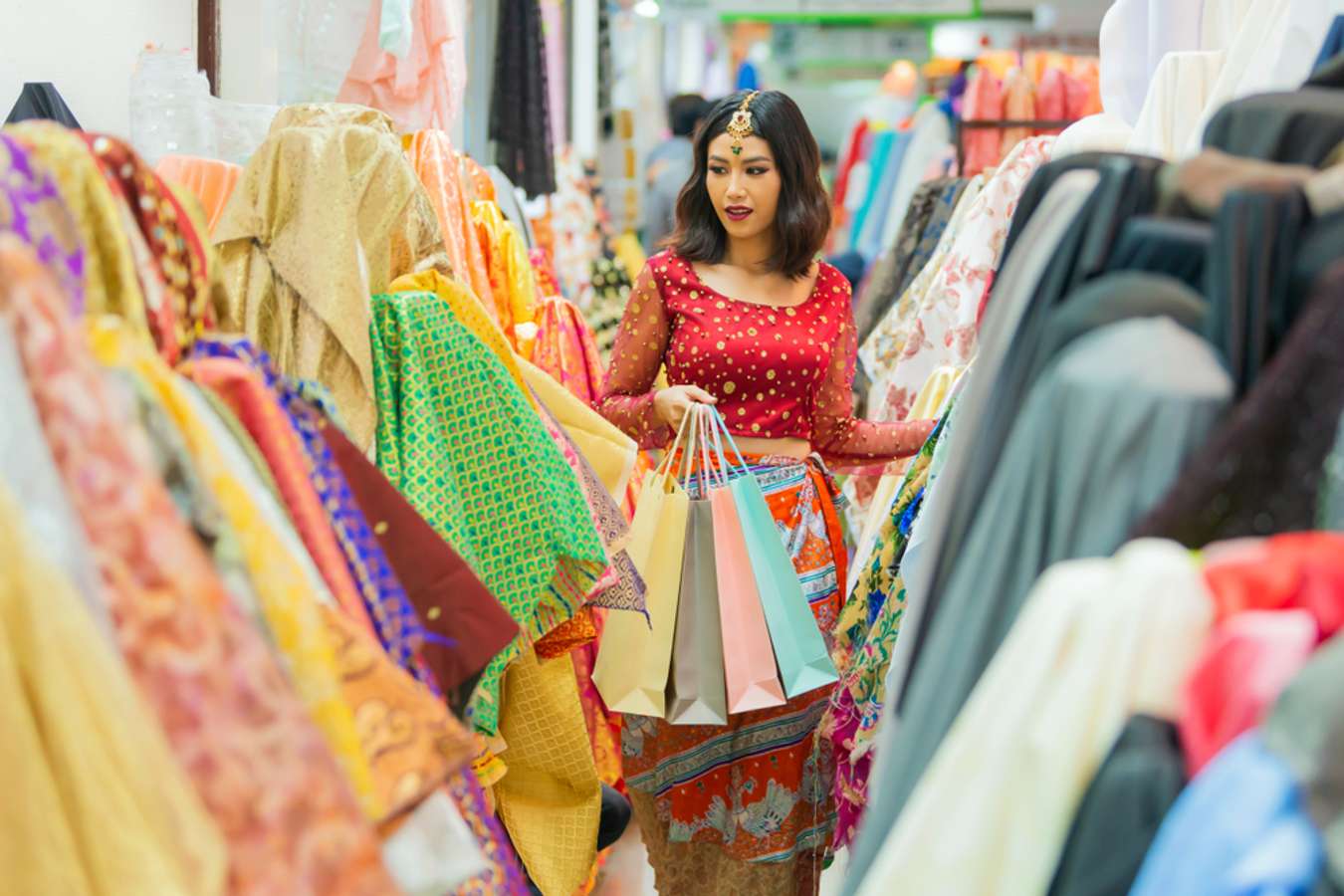 Shopping woman holding shopping bags looking fabrics of many variety in the textiles and fabrics shop. Selective focus