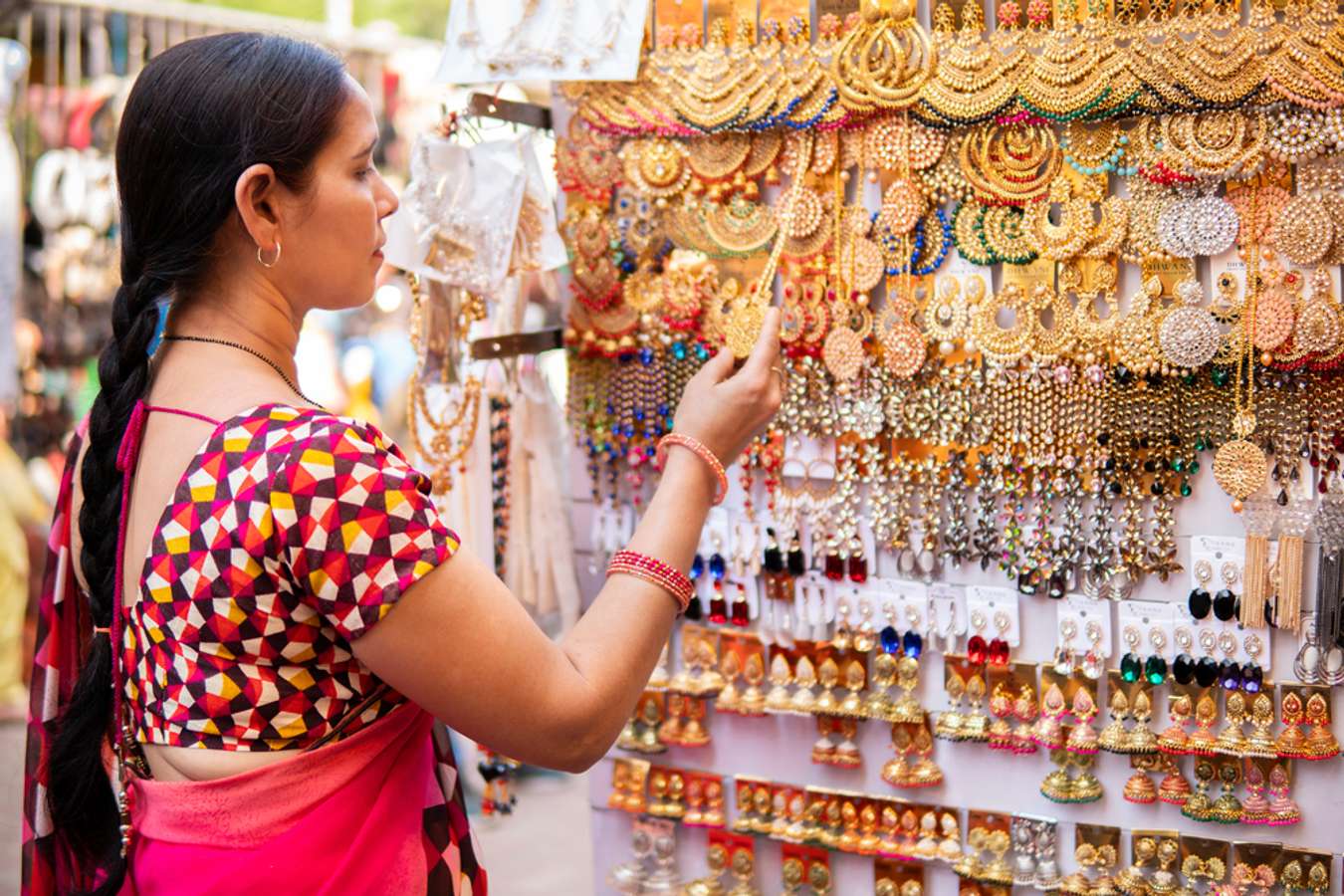 Indian mature woman looking and buying earrings, jewelry from outdoor street market of Delhi, India at day time. She is in her traditional Indian dress sari.