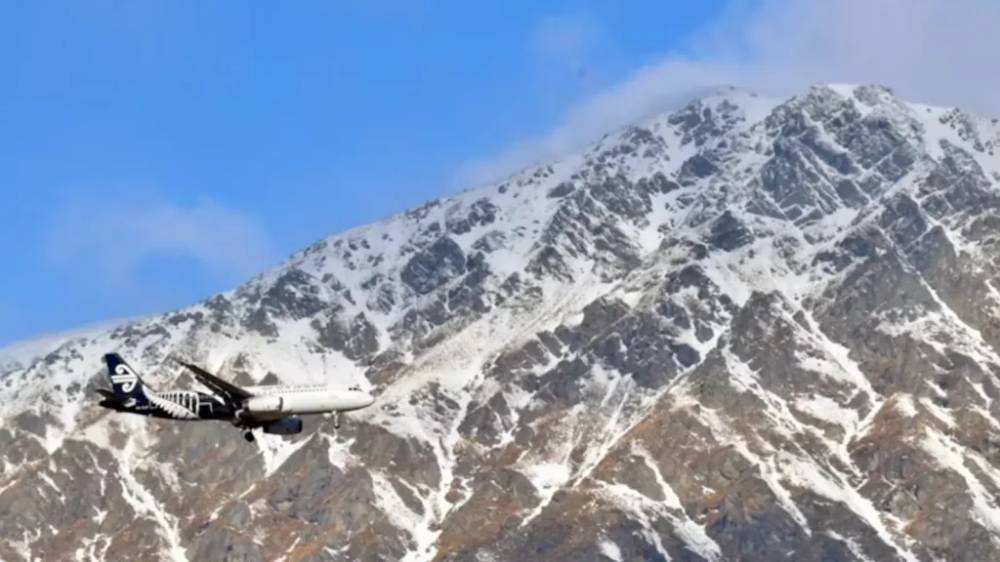 An Air New Zealand plane landing in Queenstown with a mountain in the background.