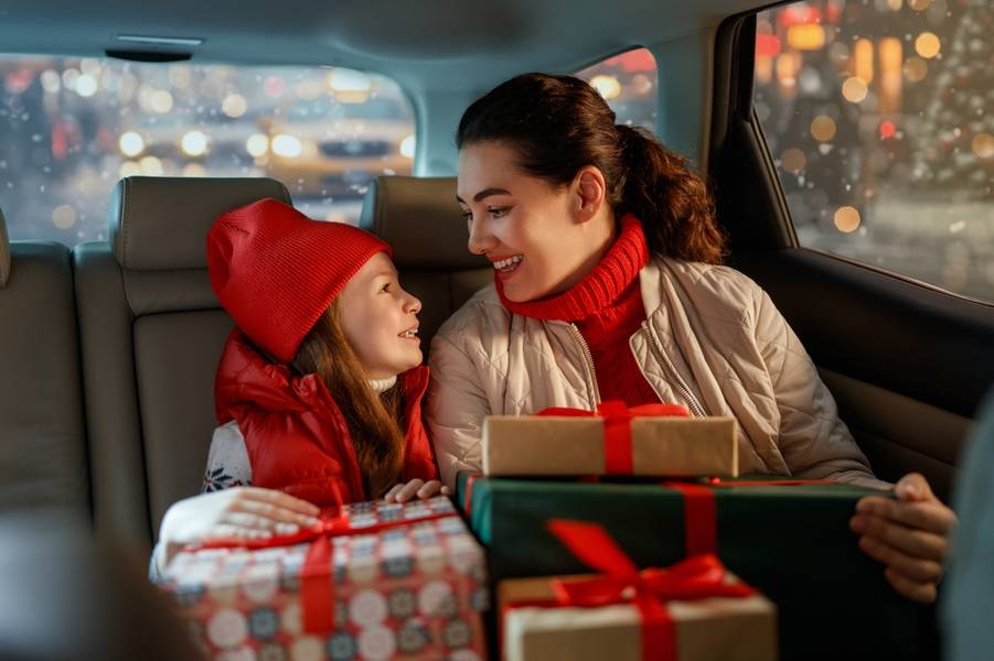 Woman and her child  holding presents and delivering them on car to home. Holidays concept. Time of Christmas Eve. 