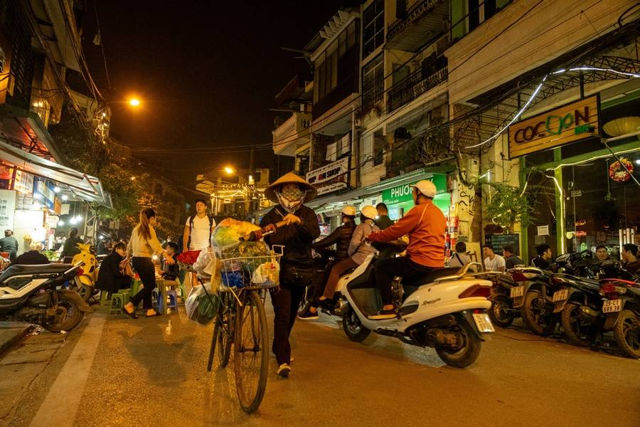 People walk and ride scooters past restaurants and food stalls in a crowded Hanoi night market, Vietnam on December 28, 2019