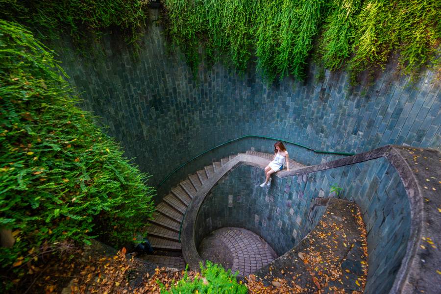 Singapore - July 28, 2018 : Young asian woman tourist sat on the staircase at Underground spiral staircase at Fort Canning Park, Landmark and popular destination in Singapore