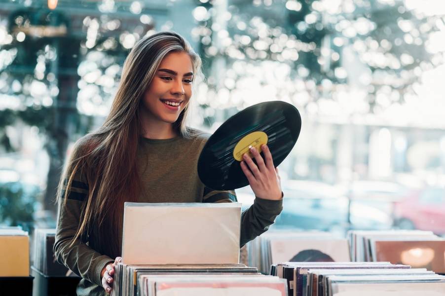 Young attractive woman holding vinyl while choosing record in a music record shop. Music addict concept. Old school classic concept.