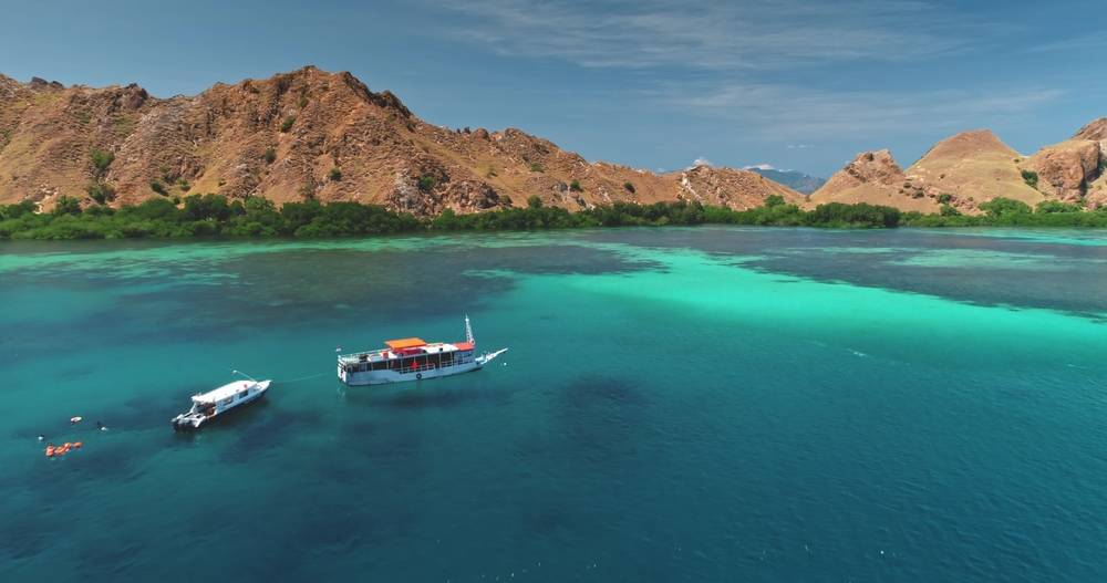 Turquoise crystal clear waters inviting exploration of coral reefs and diverse marine life around Komodo National Park, highlighting the beauty of Indonesian islands from above