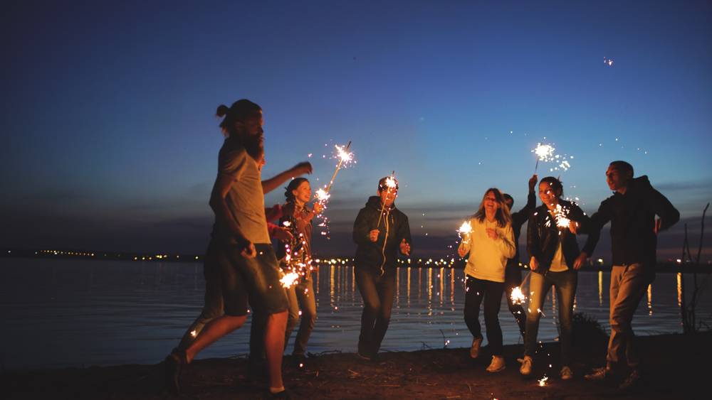 Group of young friends having a beach party. Friends dancing and celebrating with sparklers in twilight sunset