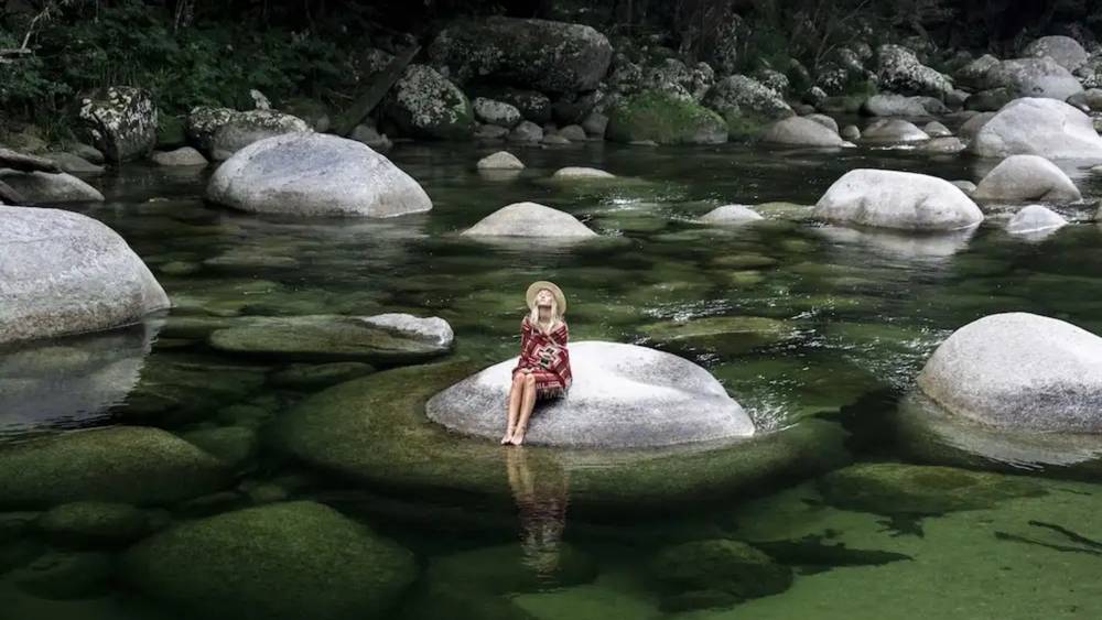 A woman sitting on a rock in the middle of a river in the Daintree Rainforest in northern Queensland, Australia.