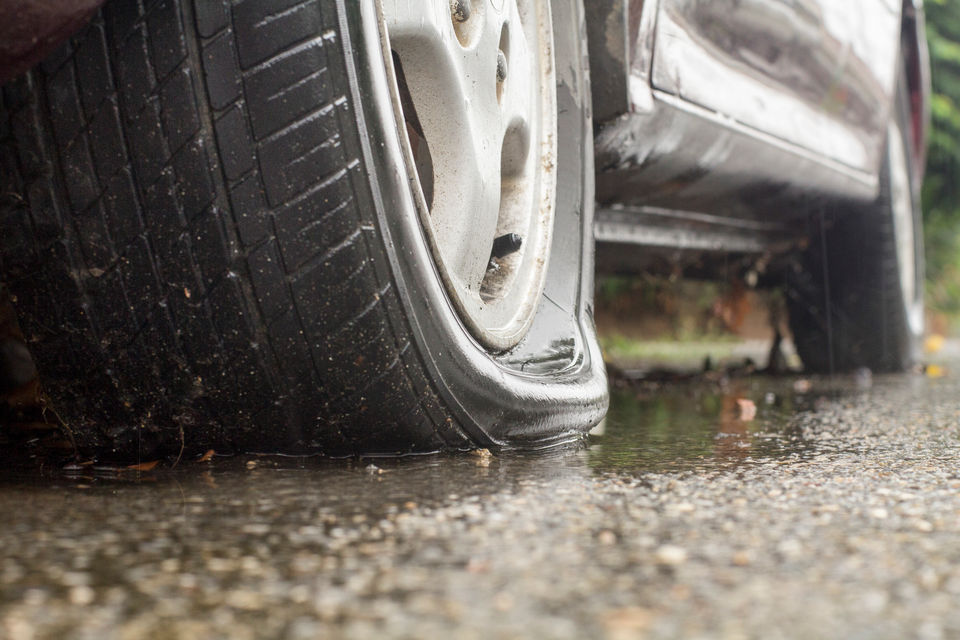 Car stuck on the side of a wet road with a flat tyre