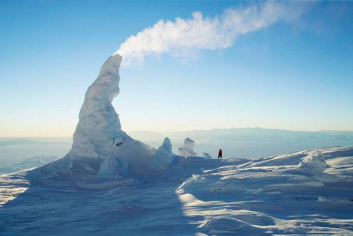 В Антарктиде есть удивительный вулкан Эребус, представляющий интерес для разных ученых. Удивительное состоит в том, что в отличие от большинства вулканов, которые после своей бурной деятельности засыпают на длительный период, Эребус действует продолжительное время. Он «включился» в 1972 году, и с тех пор не «выключался».
Есть у вулкана и другие примечательности. Две крайности, соседствующие друг с другом, лед и пламя, создают&nbsp;чудесные сооружения&nbsp;на поверхности – дымящиеся ледяные башни. Пар, выходящий наружу из недр вулкана по разломам и трещинам, в суровых условиях конденсируется и замерзает, раз за разом образуя полые строения различной формы. Глядя на эти трубы, волей-неволей сравниваешь их с дымоходами деревенских изб.
