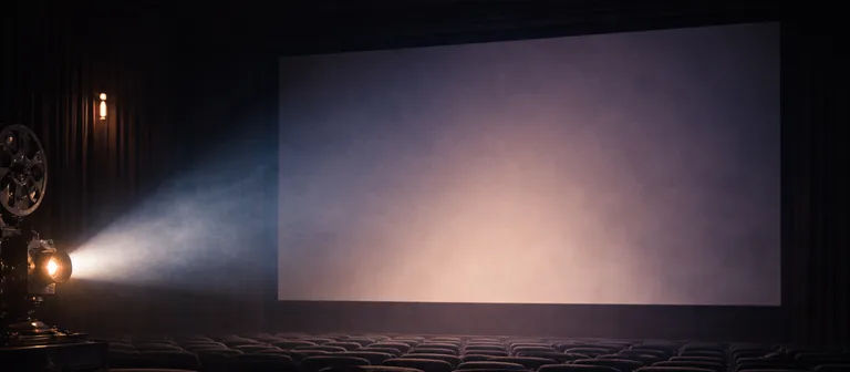 Sala de cine en penumbra con un proyector iluminando una pantalla.
