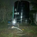 A homemade biogas production setup featuring a black storage tank connected to a small stove via pipes, demonstrating an alternative energy source for cooking.