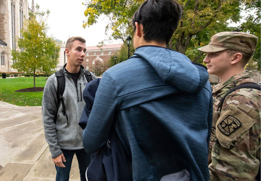 Students talking with a fellow student in military uniform on campus.