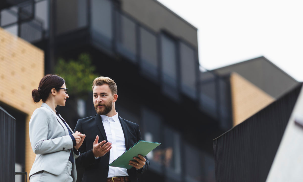 Two professionals in suits having a discussion outside a modern building.