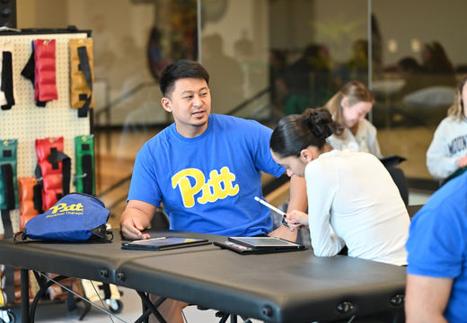 A Pitt student in a university t-shirt speaking with an attendee at a community event.